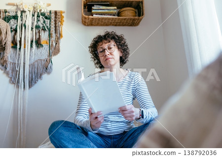 Beautiful intelligent curly haired female in her 40s with glasses reading book on bed, calm thoughtful mood, indoor routine, attractive confident woman, quiet lifestyle Beautiful intelligent curly haired female in her 40s with glasses reading book on bed, calm thoughtful mood, indoor routine, attractive confident woman, quiet lifestyle 138792036