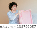 Middle aged woman holding pink sweater and inspecting result after using fabric shaver. Satisfied expression, clothing care, textile maintenance, everyday home routine, cozy interior. 138792057