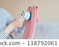 Close up female hands using fabric shaver on pink knitwear. Soft home setting, careful textile care, removing pills, everyday maintenance, cozy and mindful domestic activity. 138792061