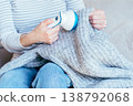 Cropped woman holding gray knitted blanket and using fabric shaver to remove pills. Sitting on sofa, casual home routine, textile care, clothing maintenance, everyday domestic activity, cozy interior. 138792068