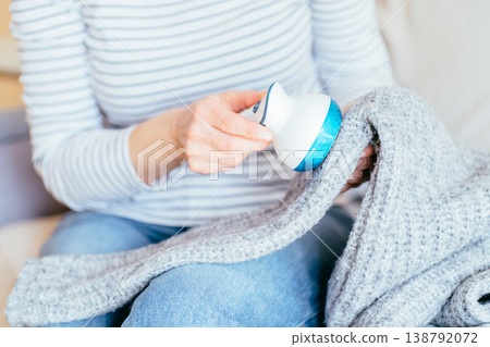 Close up of unrecognizable woman in striped shirt using fabric shaver on gray knitted sweater while sitting at home. Domestic clothing care, garment maintenance, pilling removal, cozy everyday routine Close up of unrecognizable woman in striped shirt using fabric shaver on gray knitted sweater while sitting at home. Domestic clothing care, garment maintenance, pilling removal, cozy everyday routine 138792072