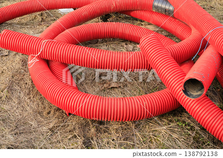 Red corrugated plastic pipes for underground cable protection at a construction site. Flexible double-wall pipes Red corrugated plastic pipes for underground cable protection at a construction site. Flexible double-wall pipes 138792138