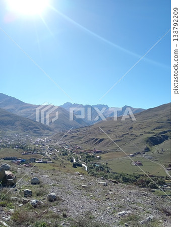 Mountain village in North Ossetia seen from above, Russia. Traditional houses and green gardens surrounded by Caucasus peaks Mountain village in North Ossetia seen from above, Russia. Traditional houses and green gardens surrounded by Caucasus peaks 138792209