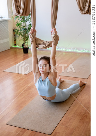Pilates workout. Sport exercise. Female laying on gym mat holding on fly yoga hammock training muscle health strength in studio interior. 138792335