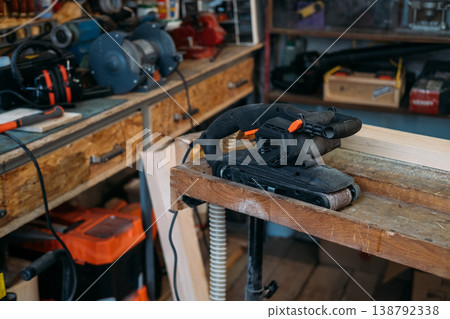 Carpentry equipment. Belt sander. Portable electric power joinery tool for woodworking near professional bench grinder in garage interior. Carpentry equipment. Belt sander. Portable electric power joinery tool for woodworking near professional bench grinder in garage interior. 138792338