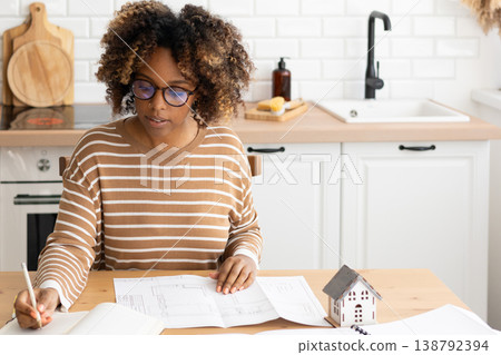 female architect designer is working, taking notes in notebook is mock up of house on table. female architect designer is working, taking notes in notebook is mock up of house on table. 138792394