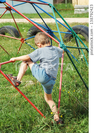 Boy conquers colorful climbing structure. Young child ascends vibrant dome with determination Boy conquers colorful climbing structure. Young child ascends vibrant dome with determination 138792423