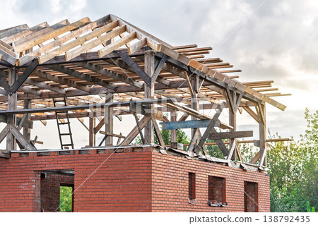 Unfinished brick building with wooden roof structure on a cloudy sky background Unfinished brick building with wooden roof structure on a cloudy sky background 138792435