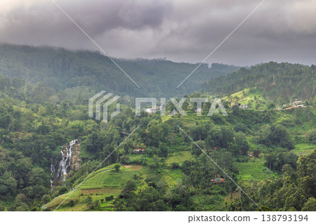 Lush Tropical Mountain Landscape with Scenic Waterfall and Verdant Hills Under Dramatic Cloudy Sky, Remote Nature Vista. Mountain landscape near Ella in Sri Lanka. Lush Tropical Mountain Landscape with Scenic Waterfall and Verdant Hills Under Dramatic Cloudy Sky, Remote Nature Vista. Mountain landscape near Ella in Sri Lanka. 138793194