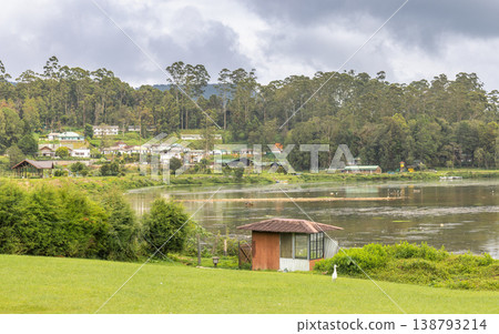 Tranquil Lakeside Village amidst Lush Green Hills and Overcast Sky, Serene Landscape with Rural Homes by Calm Water. Nuwara Eliya town in Sri Lanka. Tranquil Lakeside Village amidst Lush Green Hills and Overcast Sky, Serene Landscape with Rural Homes by Calm Water. Nuwara Eliya town in Sri Lanka. 138793214