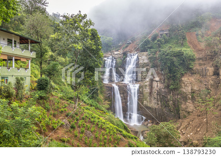 Ramboda Waterfall near Nuwara Eliya town in Sri Lanka. Misty Mountain Waterfall Landscape with Lush Green Foliage and Distant Architecture in a Serene Setting Ramboda Waterfall near Nuwara Eliya town in Sri Lanka. Misty Mountain Waterfall Landscape with Lush Green Foliage and Distant Architecture in a Serene Setting 138793230