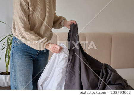 Woman taking dark duvet cover off blanket in bedroom Woman taking dark duvet cover off blanket in bedroom 138793662