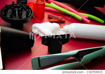 Close-up side view on a pink background, hairdryer with attachments, stylers and curling irons for straightening and creating curls, foam for volume and long-lasting, curlers in different shapes and 138793915