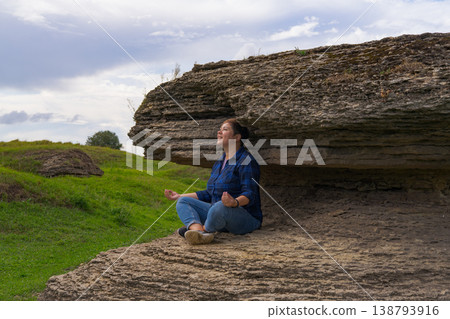 Woman in seated yoga pose beneath rocky overhang, quiet coastal scene, focused breathing, stress relief and emotional balance theme Woman in seated yoga pose beneath rocky overhang, quiet coastal scene, focused breathing, stress relief and emotional balance theme 138793916