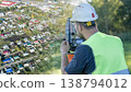 Surveyor in a hard hat and high-visibility vest uses a device 138794012