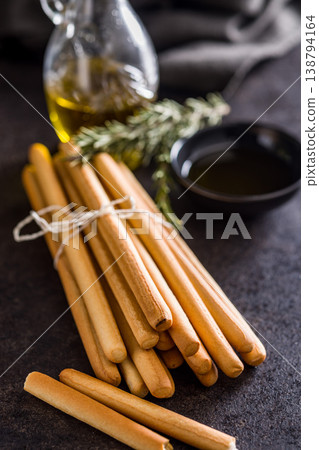 Bundled Italian Breadsticks (Grissini) with Olive Oil and Rosemary on Dark Surface 138794164