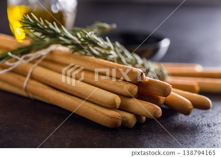 Bundled Italian Breadsticks (Grissini) with Olive Oil and Rosemary on Dark Surface Bundled Italian Breadsticks (Grissini) with Olive Oil and Rosemary on Dark Surface 138794165