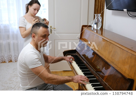 Father playing piano while teenage daughter films him and talks on mobile phone cozy family home beige room music weekend activity 138794748