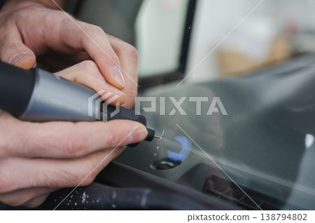 A technician drills a hole during a car windshield chip repair. A technician drills a hole during a car windshield chip repair. 138794802