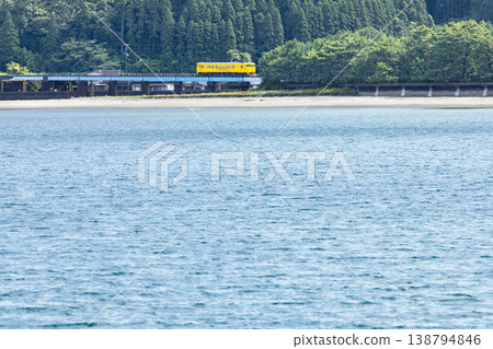 A yellow Kiha 40 train runs across a railway bridge over the Hosoda River, which flows into the Odotsu Beach in Nichinan City, Miyazaki Prefecture. 138794846