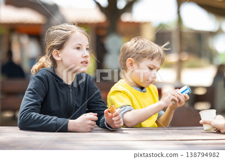Children sitting at picnic table enjoying snacks outdoors 138794982