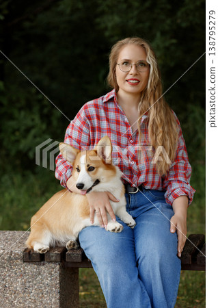 Selfassured Woman Comfortably Relaxing With Her Pet Corgi Amidst Evening Natural Scenery 138795279
