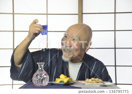 A bearded old man drinking sake in a Japanese-style room. 138795771