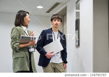 日本商界男女面帶微笑,手持筆記型電腦,站在電梯前。 日本商界男女面帶微笑,手持筆記型電腦,站在電梯前。 138795787