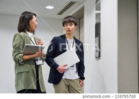 Japanese businessmen and women, smiling and holding laptops, standing in front of the elevator. 138795788
