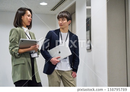 Japanese businessmen and women, smiling and holding laptops, standing in front of the elevator. 138795789