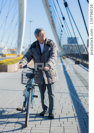 A man in his 60s walking while pushing a bicycle 138796016