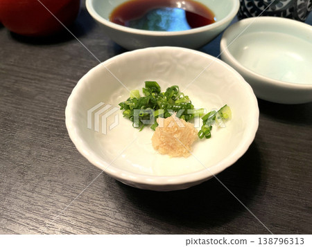 The condiments are served in a small white bowl: chopped green onions and grated ginger. 138796313