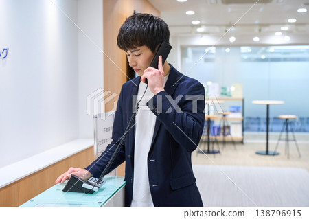 A young businessman making an internal phone call at the office reception desk. A young businessman making an internal phone call at the office reception desk. 138796915