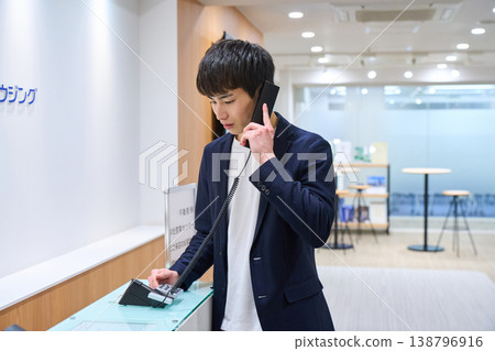 一位年輕的商人正在辦公室前台撥打內部電話。 138796916