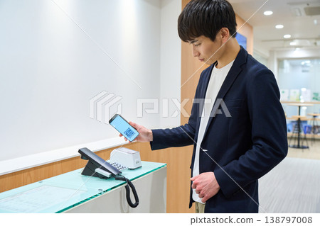 A young businessman scans a QR code on his smartphone at the office's reception system. A young businessman scans a QR code on his smartphone at the office's reception system. 138797008