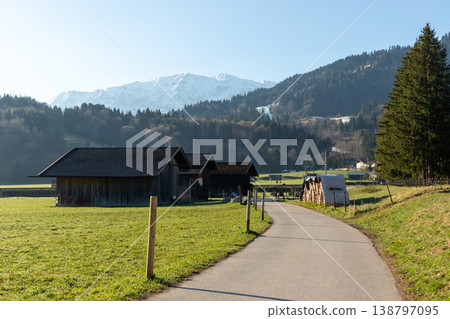 Curving rural path through meadow with barns and alpine foothills Curving rural path through meadow with barns and alpine foothills 138797095
