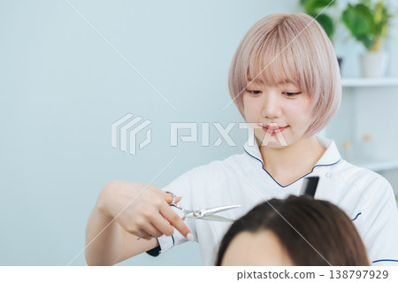 A female staff member with light-colored hair cutting hair. A female staff member with light-colored hair cutting hair. 138797929