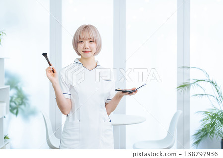 一名淺色頭髮的女工作人員手持美髮和化妝工具。 138797936
