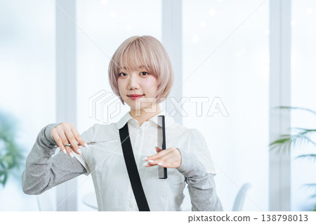 A female staff member with light-colored hair holding hair cutting tools. A female staff member with light-colored hair holding hair cutting tools. 138798013