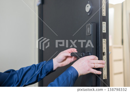 The technician installs a smart electronic lock on the front door. 138798332
