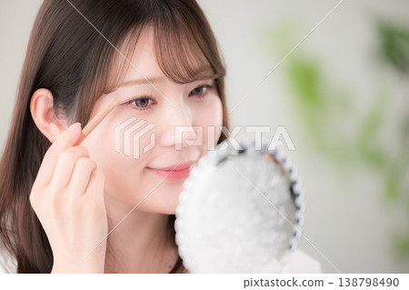 一張特寫鏡頭,一位女士對著手鏡塗抹眼影,展示了她自然的妝容和美容護理程序。 一張特寫鏡頭,一位女士對著手鏡塗抹眼影,展示了她自然的妝容和美容護理程序。 138798490