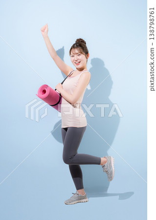 A woman holding a yoga mat against a light blue background, representing a healthy and beautiful sport, training at a gym, or lifestyle. 138798761