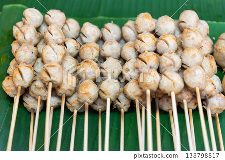 Grilled meatball skewers arranged on banana leaf juicy texture golden surface popular street food with savory flavor and simple traditional presentation Grilled meatball skewers arranged on banana leaf juicy texture golden surface popular street food with savory flavor and simple traditional presentation 138798817