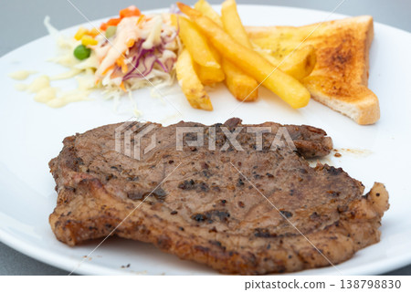 Grilled pork steak served with crispy fries toasted bread and fresh salad on white plate savory meal with juicy texture and simple presentation for restaurant menu 138798830
