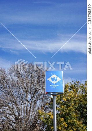 A sign indicating public Wi-Fi in Barcelona, and a view of winter trees against a blue sky. 138798850