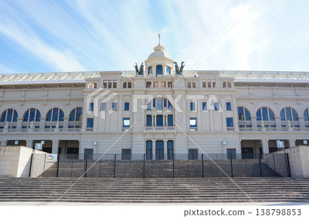 A view of a building standing under the blue sky in Barcelona, with a large staircase in front of its main entrance. 138798853