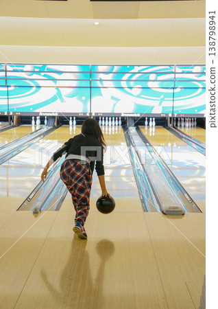 A woman's back as she enjoys bowling, in the moment of throwing the ball. A woman's back as she enjoys bowling, in the moment of throwing the ball. 138798941