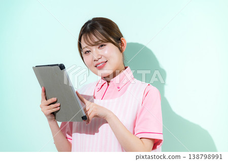 A woman working as a caregiver or childcare worker in a home care setting is shown pointing at a tablet against a green background. A woman working as a caregiver or childcare worker in a home care setting is shown pointing at a tablet against a green background. 138798991