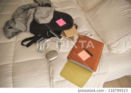 Student backpack spilling books and study items on bed Student backpack spilling books and study items on bed 138799323
