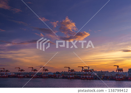 Tokyo, Japan - Oct 2 2024, Panoramic view of docks of Tokyo port with many cargo cranes lined up, colourful sunset sky with clouds, with a plane flying in sky, at evening, in gulf of Tokyo, Japan Tokyo, Japan - Oct 2 2024, Panoramic view of docks of Tokyo port with many cargo cranes lined up, colourful sunset sky with clouds, with a plane flying in sky, at evening, in gulf of Tokyo, Japan 138799412
